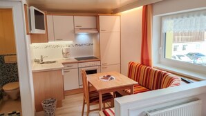 Una kitchenette compacta con microondas, cafetera y estufa. Hay una mesa de comedor con sillas y un sofá a rayas cerca de una ventana.