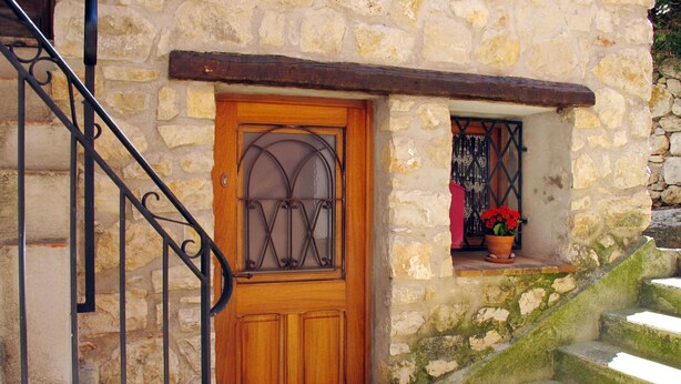 Una puerta de madera con un panel de vidrio, una pared de piedra y una pequeña ventana con una planta en maceta.