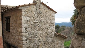 Un edificio de piedra con techo de tejas, una ventana pequeña con contraventanas y una caja de servicios.