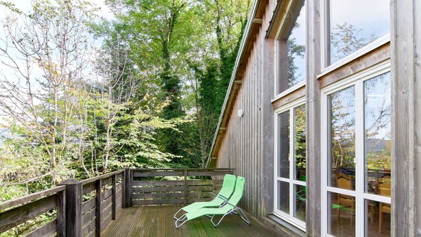 Eine Holzterrasse mit einem grünen Liegestuhl und einem Holzzaun.