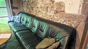 Ein schwarzes Ledersofa mit Kissen vor einer Steinwand, ein Holztisch und ein Fenster mit Blick auf Grünflächen.