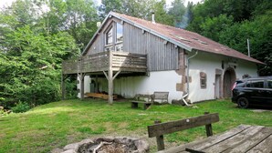 Ein rustikales Holzhaus mit geneigtem Dach, einer Veranda und einem kleinen Feuerkorb im Garten.