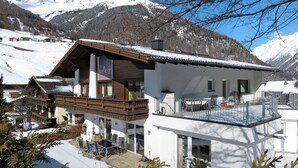 Een moderne chalet met balkon, eethoek en uitzicht op met sneeuw bedekte bergen.