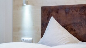 Een hotelkamer met een houten hoofdeinde, een wit kussen en een wandlamp.