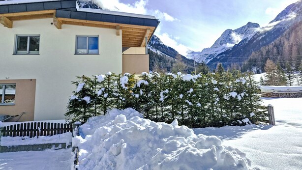 Une maison moderne à deux étages, dotée d’une façade en bois et de grandes fenêtres, entourée d’arbres et de montagnes couverts de neige.