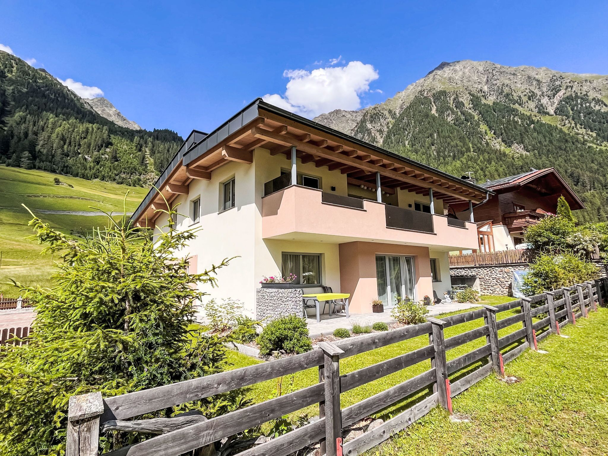 Een chalet met twee verdiepingen met een balkon, omringd door een houten hek, gelegen voor een bergachtige achtergrond.