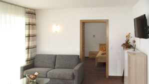 Un salon avec un canapé gris, une table basse en verre et un téléviseur fixé au mur.