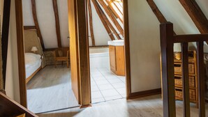 Un dormitorio estilo loft con vigas de madera a la vista, una cama litera, una silla y un baño pequeño.