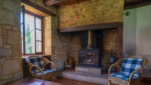 Una habitación rústica con paredes de piedra, chimenea, sillas de mimbre y una mesa de madera.