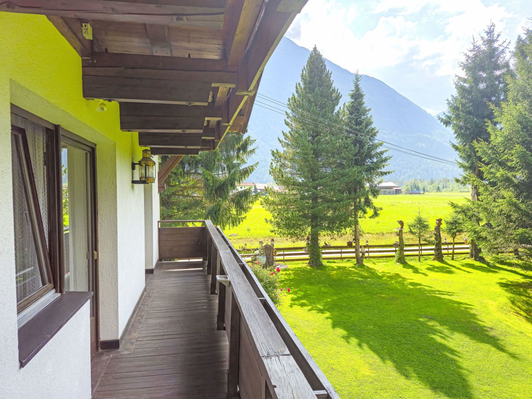 A wooden balcony with a view of a green field and mountains.