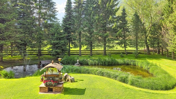 Ein friedlicher Garten mit Teich, einer Holzbank und einem rustikalen Pavillon.