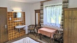Ein Zimmer mit einem Bett, einem Waschbecken, einem Spiegel, einem Tisch mit Stühlen und einem Fenster mit Vorhängen.