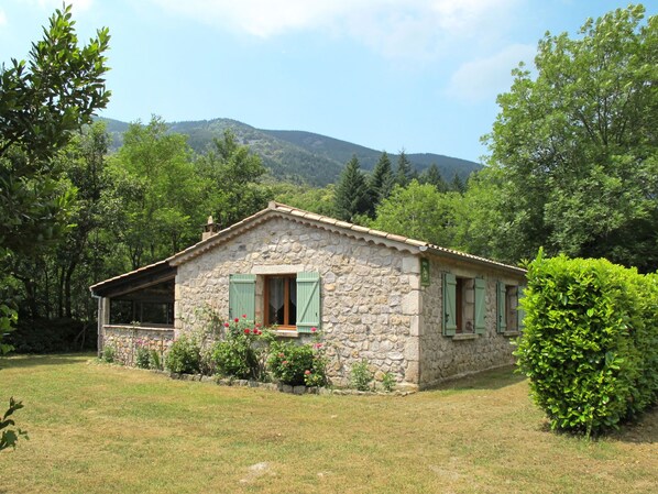 A stone house with a sloped roof, green shutters, and a small garden with flowers. - Les Galets by Interhome (Valgorge)
