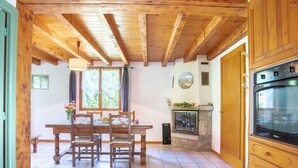 A wooden dining room with a table and chairs, a fireplace, and a kitchen area with an oven. - Les Galets by Interhome (Valgorge)