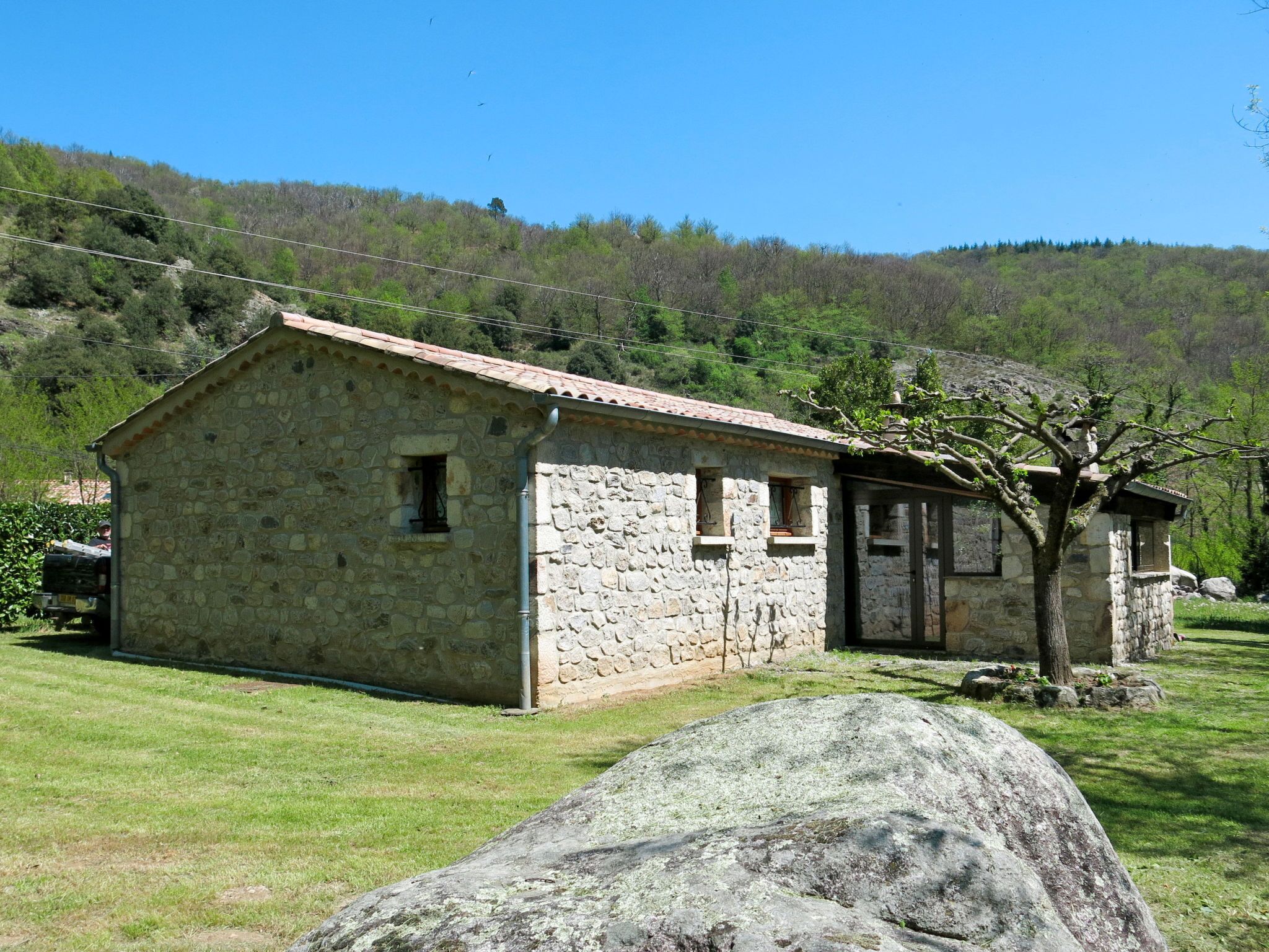 A stone building with a tiled roof, a small porch, and a tree in the foreground.