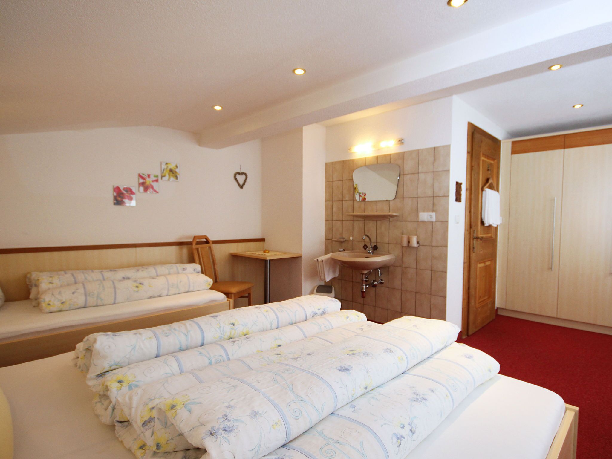 Una habitación de hotel con dos camas, una mesita, un lavamanos y un espejo.