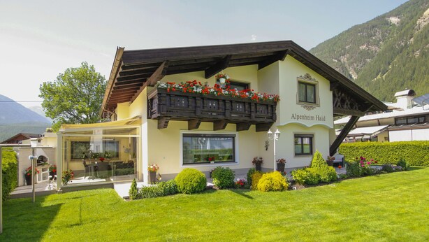 A two-story building with a balcony adorned with flowers, a sign reading "Alpenheim Haus," and a well-maintained garden. - Alpenheim Haid by Interhome (Längenfeld)