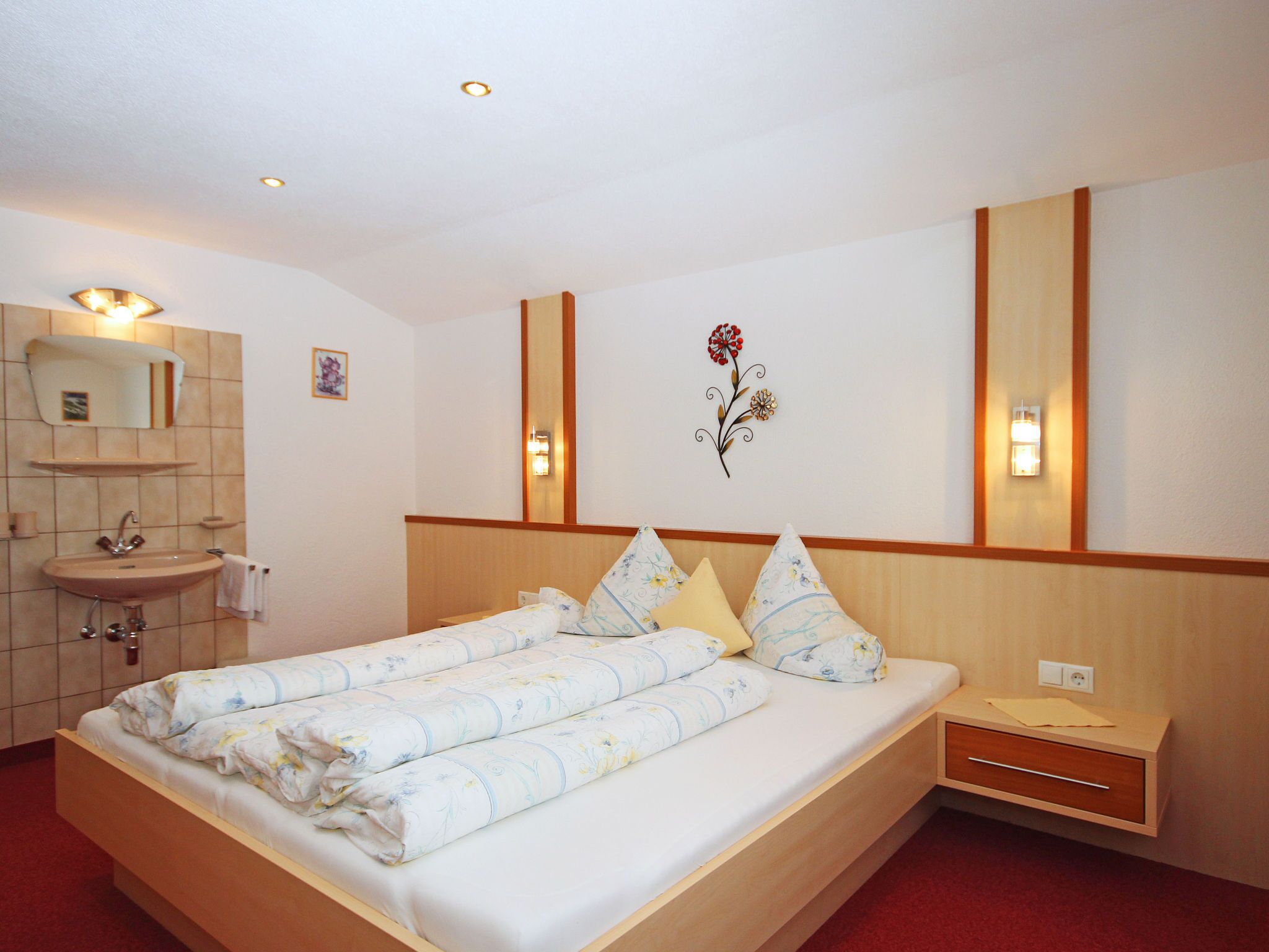 A hotel room with a bed, a nightstand, a sink, and a mirror.