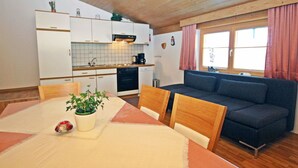 A compact living space with a dining table, chairs, a sofa, a kitchen area with cabinets and appliances, and a window with curtains. - Alpenheim Haid by Interhome (Längenfeld)