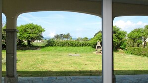A covered patio with stone flooring, a view of a grassy yard with a stone structure, and trees in the background. - La Jolie Vague by Interhome (Baubigny)