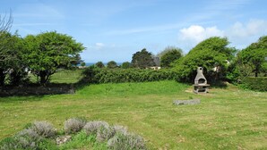 A grassy field with a stone structure, possibly a barbecue area, surrounded by trees and a clear sky. - La Jolie Vague by Interhome (Baubigny)