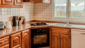 A kitchen with wooden cabinets, a gas stove, a dishwasher, and a window with curtains. - La Jolie Vague by Interhome (Baubigny)