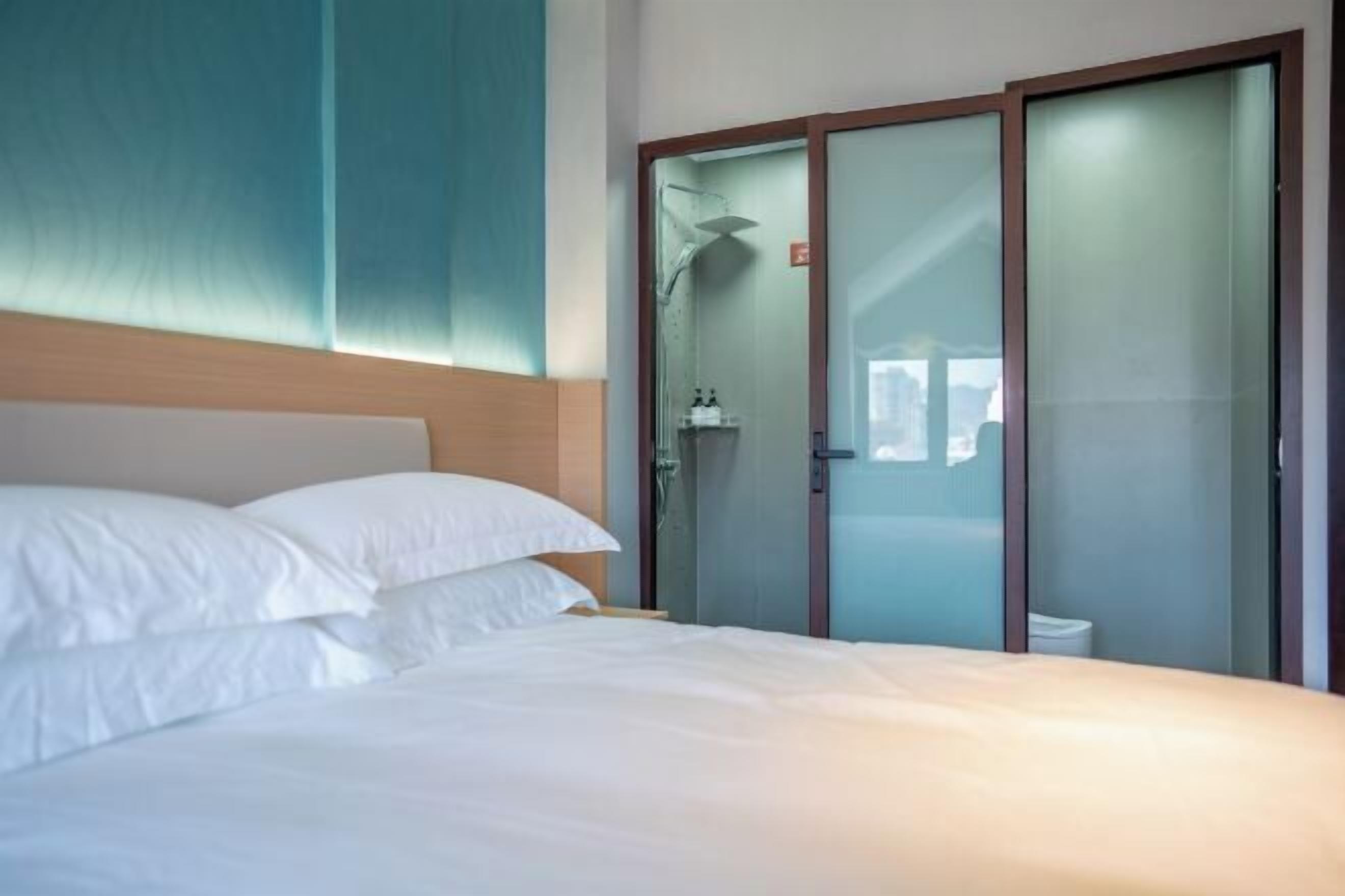 A hotel room with a bed, a shower, and a glass door closet.