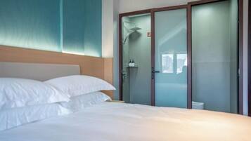 A hotel room with a bed, a shower, and a glass door closet.
