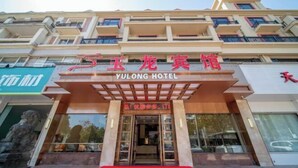 The exterior of Yulong Hotel with a red carpet entrance, a large glass facade, and a statue on the left. - Yulong Hostel (Xianju)