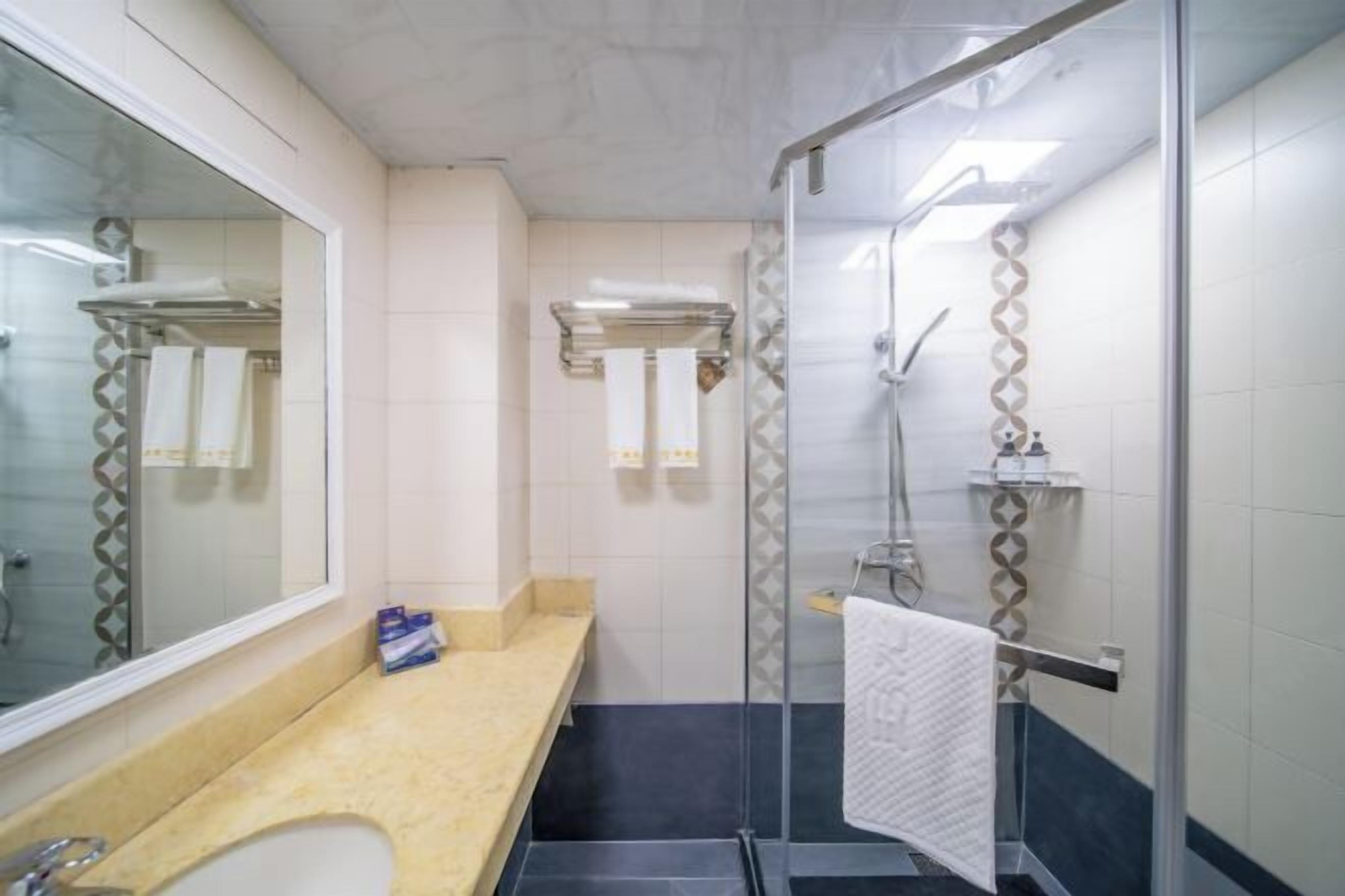 A bathroom with a glass shower enclosure, a sink with a beige countertop, and a mirror.