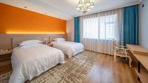 A hotel room with two beds, a desk, a chair, a patterned rug, and a chandelier. - Yulong Hostel (Xianju)