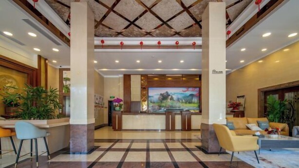 A hotel lobby with a reception desk, seating area, and a large screen. - Yulong Hostel (Xianju)