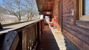 Eine Holzhütte mit überdachter Veranda und Blick auf die umliegende Landschaft, mit einem Schild, das eine Sauna anwirbt.