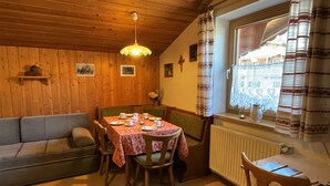 Ein gemütlicher Essbereich mit einem Tisch für vier Personen, Holzwänden, Holzbalkendecke und einem fenster mit Vorhängen.