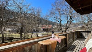 Eine Holzterrasse mit Tisch für zwei Personen, mit Blick auf eine ländliche Landschaft mit Bäumen und Häusern.