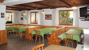 Comedor con bancos y mesas de madera, televisor y ventanas con cortinas.