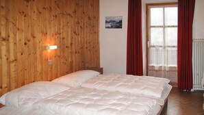 Habitación con paneles de madera, una cama, una lámpara de pared, un ventanal con cortinas rojas y un radiador.