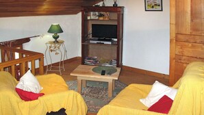 Een gezellige woonkamer met twee gele fauteuils, een houten salontafel, een televisie en een klein bijzettafeltje met een lamp.