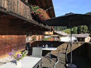 An outdoor patio with a table and chairs, a hanging flower basket, and a view of the surrounding area.
