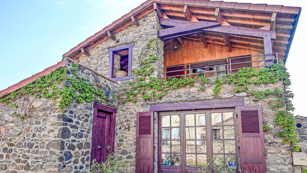 A stone building with a wooden balcony, purple shutters, and potted plants.
