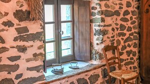 A rustic room with a stone wall, a wooden chair, and a window with shutters.