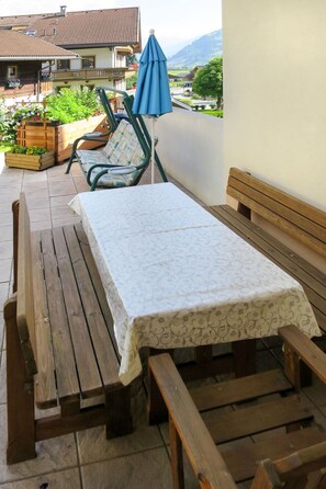 A wooden bench and table set on a patio with a view of houses and mountains. - Apartment Holaus by Interhome (Mayrhofen)
