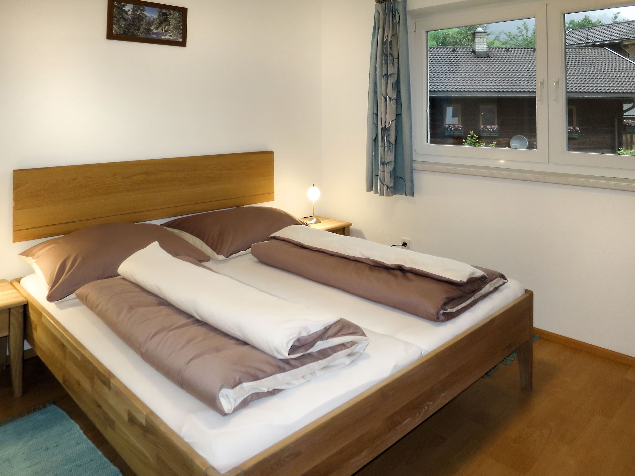 Un lit double avec une tête de lit en bois, une table de chevet avec une lampe et une fenêtre avec des rideaux.