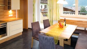 Une cuisine moderne avec des meubles en bois, un four encastré et un coin repas comprenant une table en bois, des chaises et un panier de fruits.