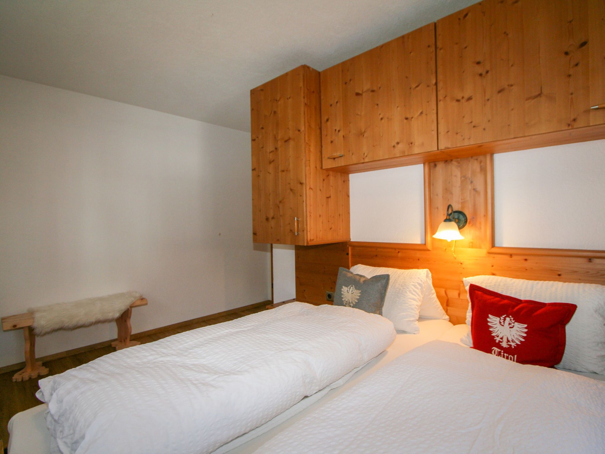 Un dormitorio con dos camas, cabeceros de madera, ropa de cama blanca y una mesita de noche con lámpara.