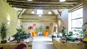 Un interior rústico con vigas de madera a la vista, una zona de estar central con sillas de colores y una variedad de plantas en macetas.