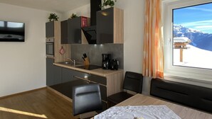 Eine moderne Küche mit eingebautem Herd, Spüle und Kaffeemaschine. Ein Essbereich mit Tisch und Stühlen lädt zum Verweilen ein, und ein Fenster bietet Blick auf die Berge.