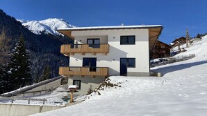 Eine moderne, zweistöckige Chalet mit Holzbalkonen vor einer verschneiten Berglandschaft.