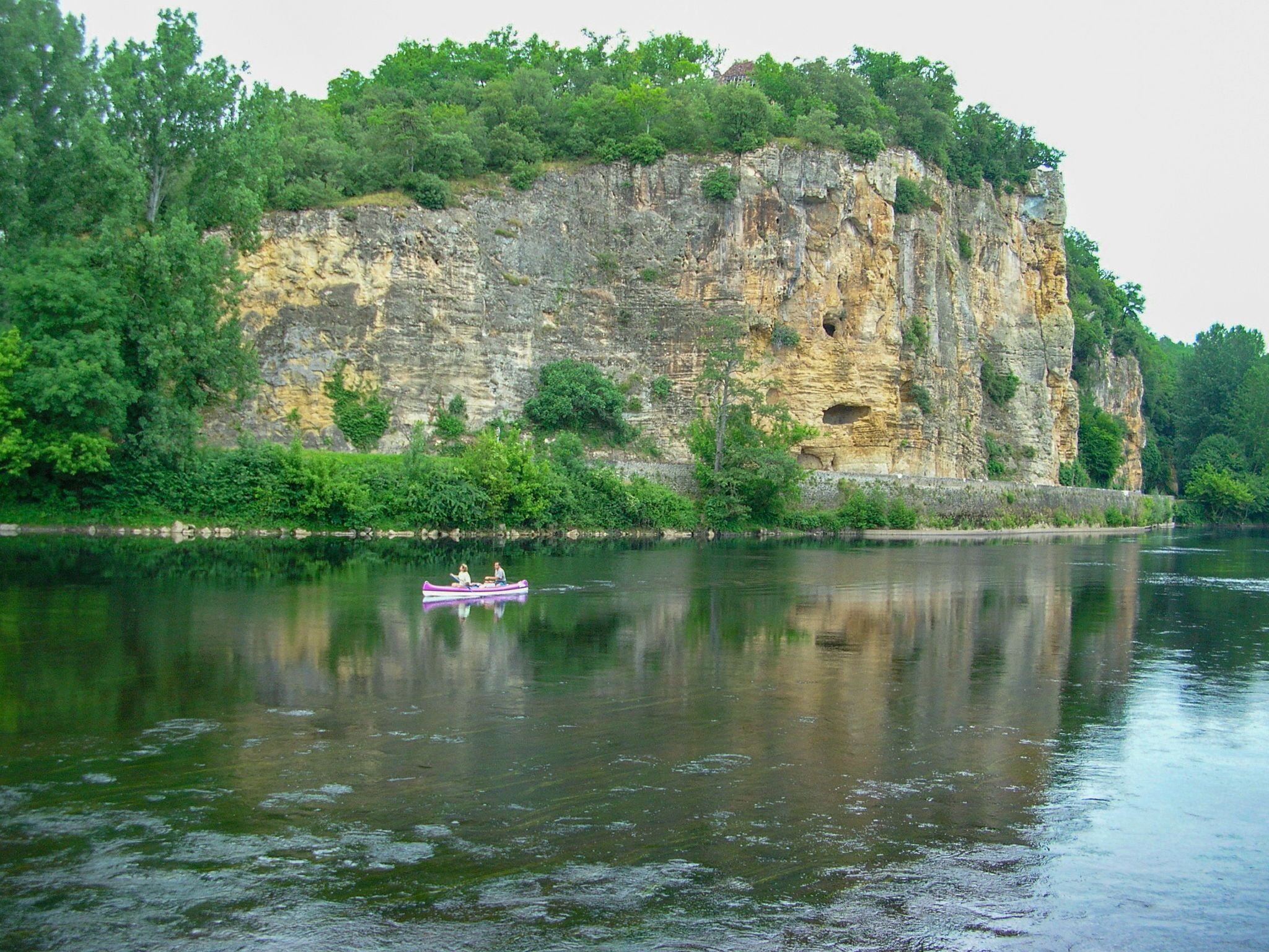 Um rio calmo com um penhasco rochoso e vegetação densa.