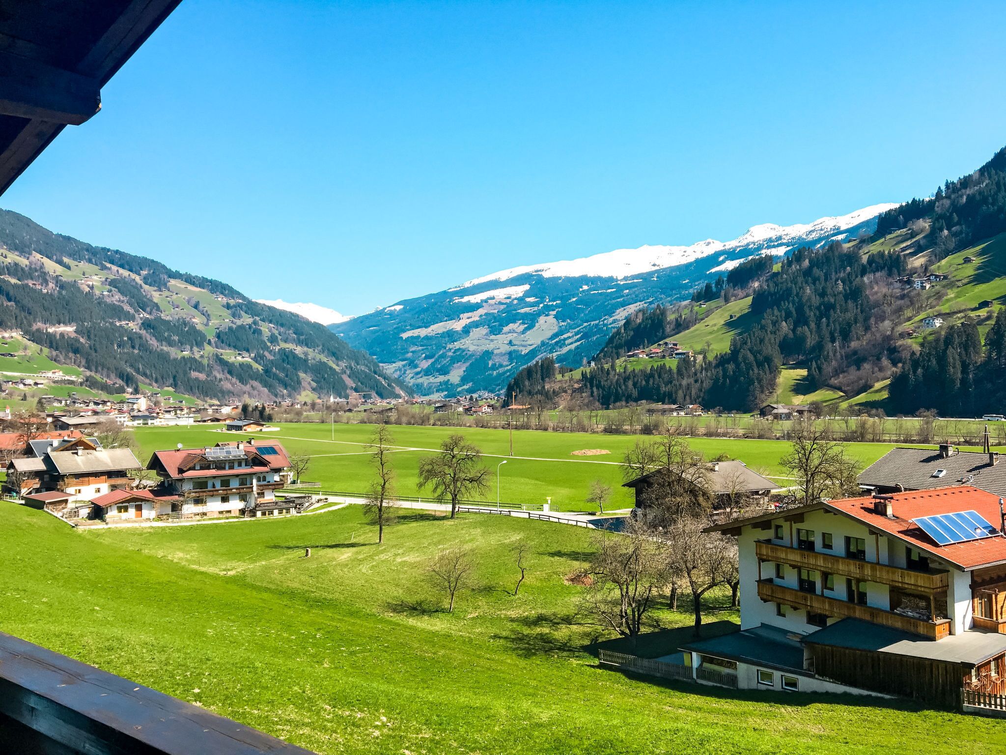 Vista de un pueblo de montaña con casas tradicionales, un valle verde y montañas nevadas al fondo.